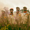 Six men in boiler suits standing in front of a mill.