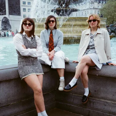 IN CONVERSATION: Girl Ray "Prestige was made to be a dazzling party in your headphones. An album to listen to striding down the street." 32 Girl Ray sitting on a wall wearing sunglasses.